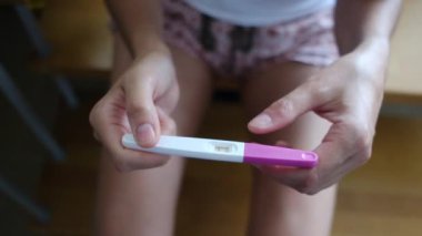 Hamilelik testi olan genç bir kadın, sonuçları kontrol ediyor, sabahları evde oturuyor. Hamilelik, sağlık