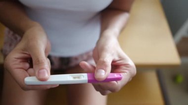 Hamilelik testi olan genç bir kadın, sonuçları kontrol ediyor, sabahları evde oturuyor. Hamilelik, sağlık
