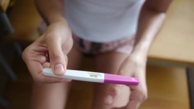 Hamilelik testi olan genç bir kadın, sonuçları kontrol ediyor, sabahları evde oturuyor. Hamilelik, sağlık