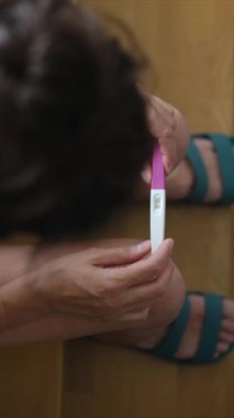 Hamilelik testi olan genç bir kadın, sonuçları kontrol ediyor, sabahları evde oturuyor. Hamilelik, sağlık