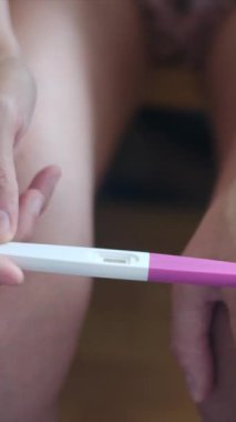 Hamilelik testi olan genç bir kadın, sonuçları kontrol ediyor, sabahları evde oturuyor. Hamilelik, sağlık