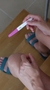 Hamilelik testi olan genç bir kadın, sonuçları kontrol ediyor, sabahları evde oturuyor. Hamilelik, sağlık