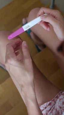 Hamilelik testi olan genç bir kadın, sonuçları kontrol ediyor, sabahları evde oturuyor. Hamilelik, sağlık