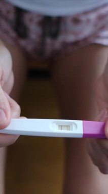Hamilelik testi olan genç bir kadın, sonuçları kontrol ediyor, sabahları evde oturuyor. Hamilelik, sağlık