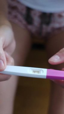 Hamilelik testi olan genç bir kadın, sonuçları kontrol ediyor, sabahları evde oturuyor. Hamilelik, sağlık