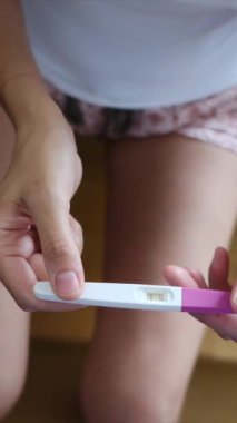 Hamilelik testi olan genç bir kadın, sonuçları kontrol ediyor, sabahları evde oturuyor. Hamilelik, sağlık