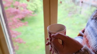 Kadın pencerenin önünde dikilirken aromatik kahve içiyor.