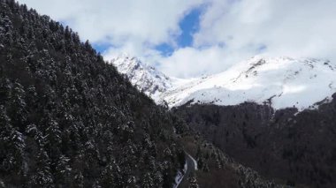 Hava aracı videosu, bulutlu bir havada, kar örtüsü zirvesi olan görkemli dağları görüntülüyor. 