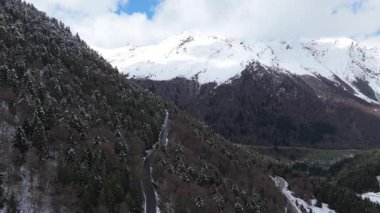 Hava aracı videosu, bulutlu bir havada, kar örtüsü zirvesi olan görkemli dağları görüntülüyor. 