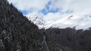 Hava aracı videosu, bulutlu bir havada, kar örtüsü zirvesi olan görkemli dağları görüntülüyor. 