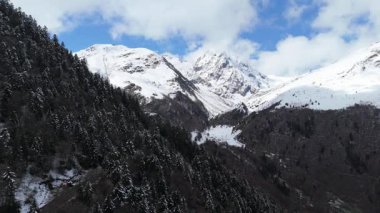 Hava aracı videosu, bulutlu bir havada, kar örtüsü zirvesi olan görkemli dağları görüntülüyor. 