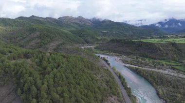 Yavaşça uçan dron görkemli dağlar, nehir, ağaçlar ve bulutlu gökyüzünü yakalıyor. 
