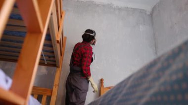 Kırmızı tişörtlü bir kadın yüz maskesi takıyor ve duvarları kontrol ediyor. 