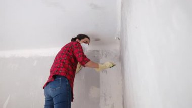 Kırmızı gömlekli bir kadın, maske takıyor, yenilenmiş bir dairede duvarları yıkıyor. 