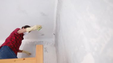 Kırmızı gömlekli yüz maskesi takan ve yenileme dairesinde duvarları yıkayan bir kadın. Yavaş çekim videosu.