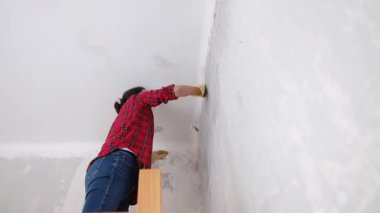 Kırmızı gömlekli bir kadın, maske takıyor, yenilenmiş bir dairede duvarları yıkıyor. 