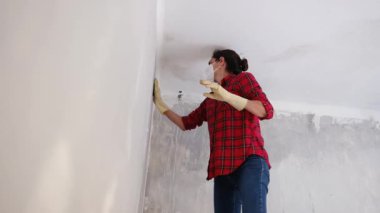 Kırmızı gömlekli bir kadın, maske takıyor, yenilenmiş bir dairede duvarları yıkıyor. 