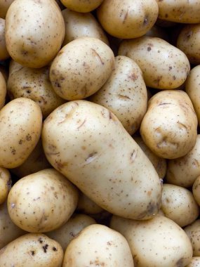 Bir demet çiğ, soyulmamış patates, çeşitli tariflerde kullanılmaya hazır. Görüntü, patatesin dokusunu ve çeşitliliğini vurgular, yemek pişirmede kullanılmak için idealdir ya da yemekle ilgili bir arka plan olarak 