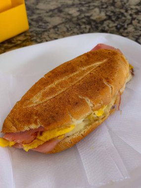 Jambonlu peynirli sandviçin iştahı kabuklu ekmeğin üzerinde. Görüntü ekmeğin dokusunu, lezzetli jambonu, erimiş peyniri ve mükemmel pişirilmiş yumurtayı ön plana çıkarıyor..