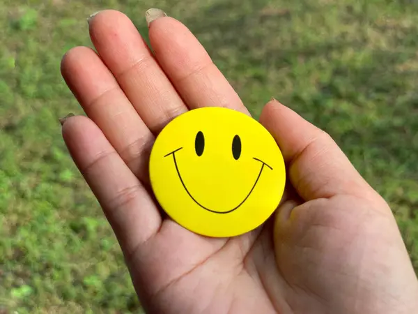 Motivational and inspirational image. Yellow smiley face on a palm. With blurred styled background.