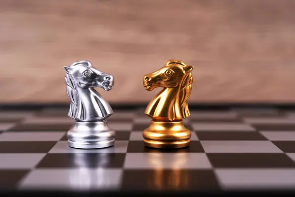 Motivational business and management concept. A pair of silver and gold chess knights facing each other.