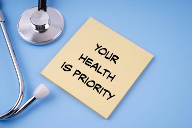 Motivational health and medical concept.YOUR HEALTH IS PRIORITY written on a paper. On blue background.