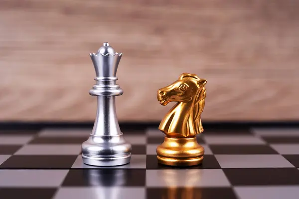 Motivational business and management concept. A silver bishop and gold knight pieces placed on a chessboard.