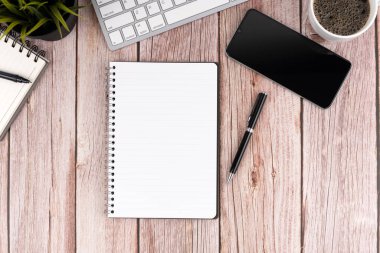 Bir dizüstü bilgisayar, defterler, bir kalem, bir cep telefonu, bir fincan kahve ve ahşap bir masanın üzerinde saksı yeşil bir bitki.