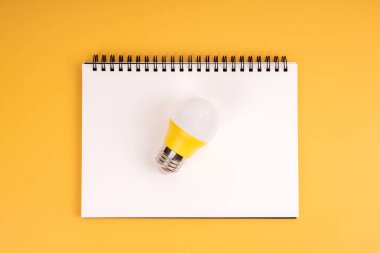 Bir ampul ve sarı arkaplanda boş bir defter.