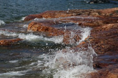 Eira, Helsinki, Finlandiya 'da birçok küçük dalgalar kırmızı ve siyah plaj kayalarını vurur. Baltık Denizi kıyısında güneşli bir yaz günü. Renkli görüntü doğanın gücünü, denizi ve temiz İskandinav şehir doğasını gösteriyor..
