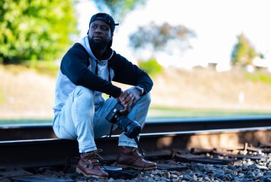 Tren raylarında oturan siyah şapkalı ve kameralı bir adam.