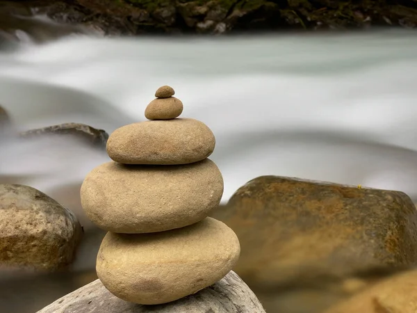 Stack of balanced stones close up with long exposure of water river background.