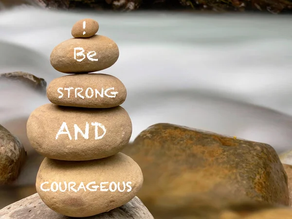 Inspirational Motivational Quote. Be strong and courageous text on rock background.