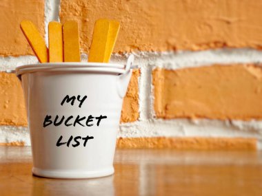 Inspirational and conceptual - My bucket list text on a white pail with orange color background. With wooden sticks for copy space. clipart