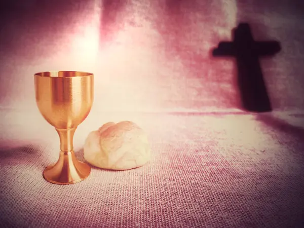 Maundy Thursday, Lent, Holy Week, Easter concept - chalice of wine, bread and blurry cross shape in red purple vintage background.