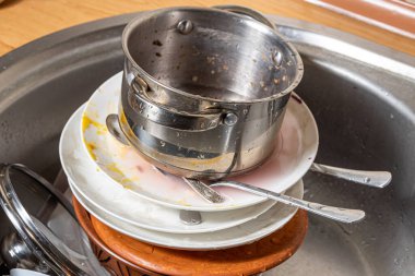 Lavaboda kirli bulaşık yığını var. Mutfakta karışıklık. Kirli mutfak eşyaları, tabaklar ve kupalar. Tembellik. Dağınık daire. Çatal bıçak takımı ve bulaşık takımı.