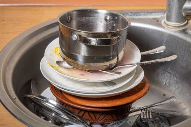 Lavaboda kirli bulaşık yığını var. Mutfakta karışıklık. Kirli mutfak eşyaları, tabaklar ve kupalar. Tembellik. Dağınık daire. Çatal bıçak takımı ve bulaşık takımı.