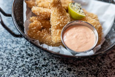 Lezzetli bir hamurun içine yerleştirilmiş, Panko ile çıtır çıtır olmuş ve masanın üstündeki tabağa yakın sosa sarılmış tavuk külçeleri..