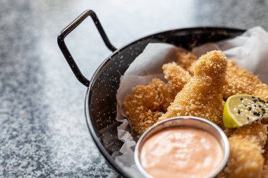 Lezzetli bir hamurun içine yerleştirilmiş, Panko ile çıtır çıtır olmuş ve masanın üstündeki tabağa yakın sosa sarılmış tavuk külçeleri..