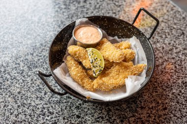 Lezzetli bir hamurun içine yerleştirilmiş, Panko ile çıtır çıtır olmuş ve masanın üstündeki tabağa yakın sosa sarılmış tavuk külçeleri..