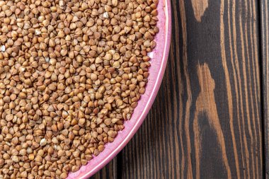 Buckwheat Grains on Plate on Wooden Background, Top View, Copy Space.Hulled kernels of buckwheat grains close up. Food background. clipart