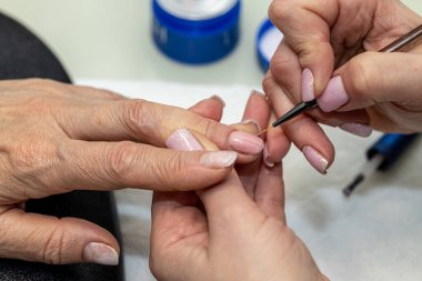 Güzellik salonunda çivi bakım prosedürü. Kadın eli ve manikür aletleri, güzellik salonunda manikür yapma süreci. Spa vücut bakımı kavramı. Tırnak etlerini kesen yetenekli bir manikürcünün eldivenli elleri.