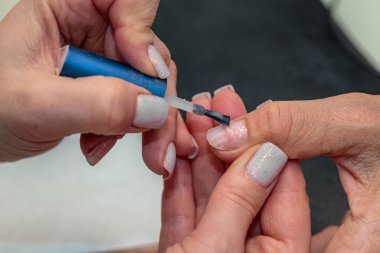 Güzellik salonunda çivi bakım prosedürü. Kadın eli ve manikür aletleri, güzellik salonunda manikür yapma süreci. Spa vücut bakımı kavramı. Tırnak etlerini kesen yetenekli bir manikürcünün eldivenli elleri.