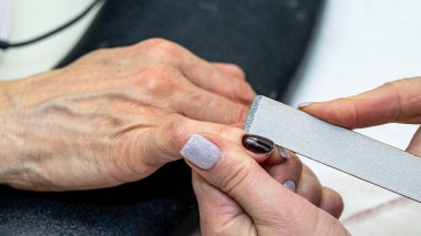 Güzellik salonunda çivi bakım prosedürü. Kadın eli ve manikür aletleri, güzellik salonunda manikür yapma süreci. Spa vücut bakımı kavramı. Tırnak etlerini kesen yetenekli bir manikürcünün eldivenli elleri.