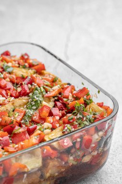 Akdeniz usulü kavrulmuş sebzeler, beyaz rustik bir masada, malzemelerle birlikte salata kasesinde. Beyaz arka planda kapari ve zeytinlerle kızartılmış sarı ve kırmızı biber salatası. Izgara sebze..