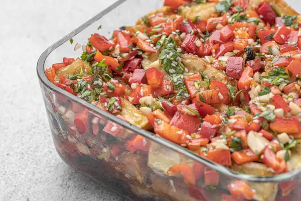 Akdeniz usulü kavrulmuş sebzeler, beyaz rustik bir masada, malzemelerle birlikte salata kasesinde. Beyaz arka planda kapari ve zeytinlerle kızartılmış sarı ve kırmızı biber salatası. Izgara sebze..