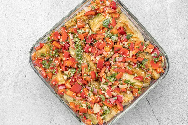 Akdeniz usulü kavrulmuş sebzeler, beyaz rustik bir masada, malzemelerle birlikte salata kasesinde. Beyaz arka planda kapari ve zeytinlerle kızartılmış sarı ve kırmızı biber salatası. Izgara sebze..