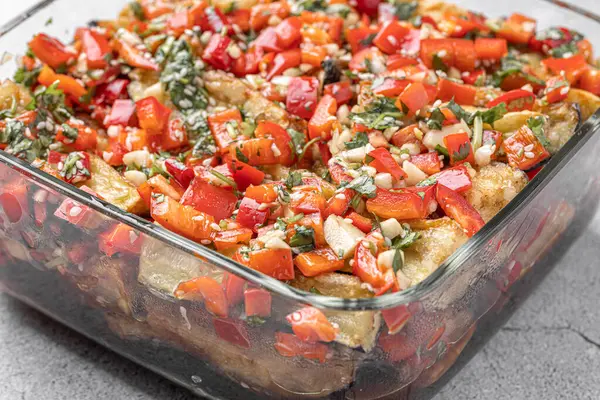 Akdeniz usulü kavrulmuş sebzeler, beyaz rustik bir masada, malzemelerle birlikte salata kasesinde. Beyaz arka planda kapari ve zeytinlerle kızartılmış sarı ve kırmızı biber salatası. Izgara sebze..