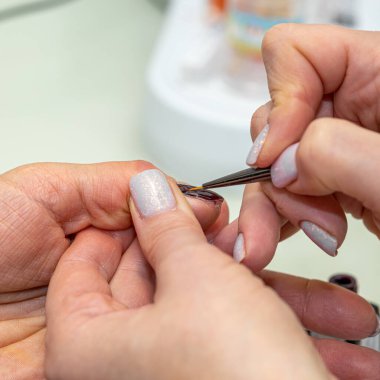 Güzellik salonunda çivi bakım prosedürü. Kadın eli ve manikür aletleri, güzellik salonunda manikür yapma süreci. Spa vücut bakımı kavramı. Tırnak etlerini kesen yetenekli bir manikürcünün eldivenli elleri.
