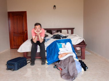 At kuyruklu bir adam odasında oturmuş kıyafetlerinin ve bavulunun nasıl dağınık olduğunu ve yere fırlatıldığını izliyor.